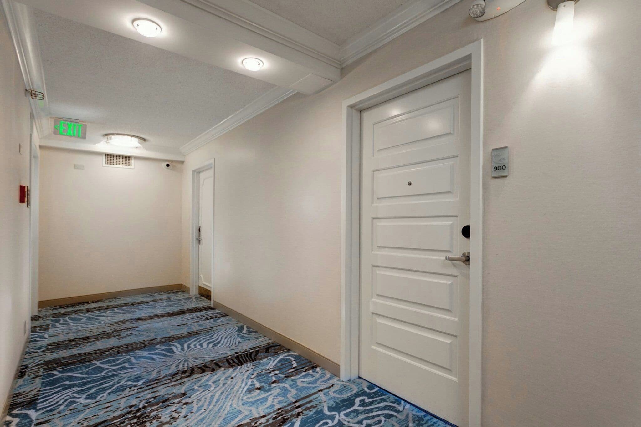 Un pasillo de hotel con alfombra estampada, puertas blancas y luces en el techo.