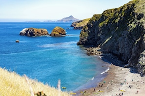 Un paisaje costero con aguas azul cristalino, acantilados rocosos y una playa arenosa.
