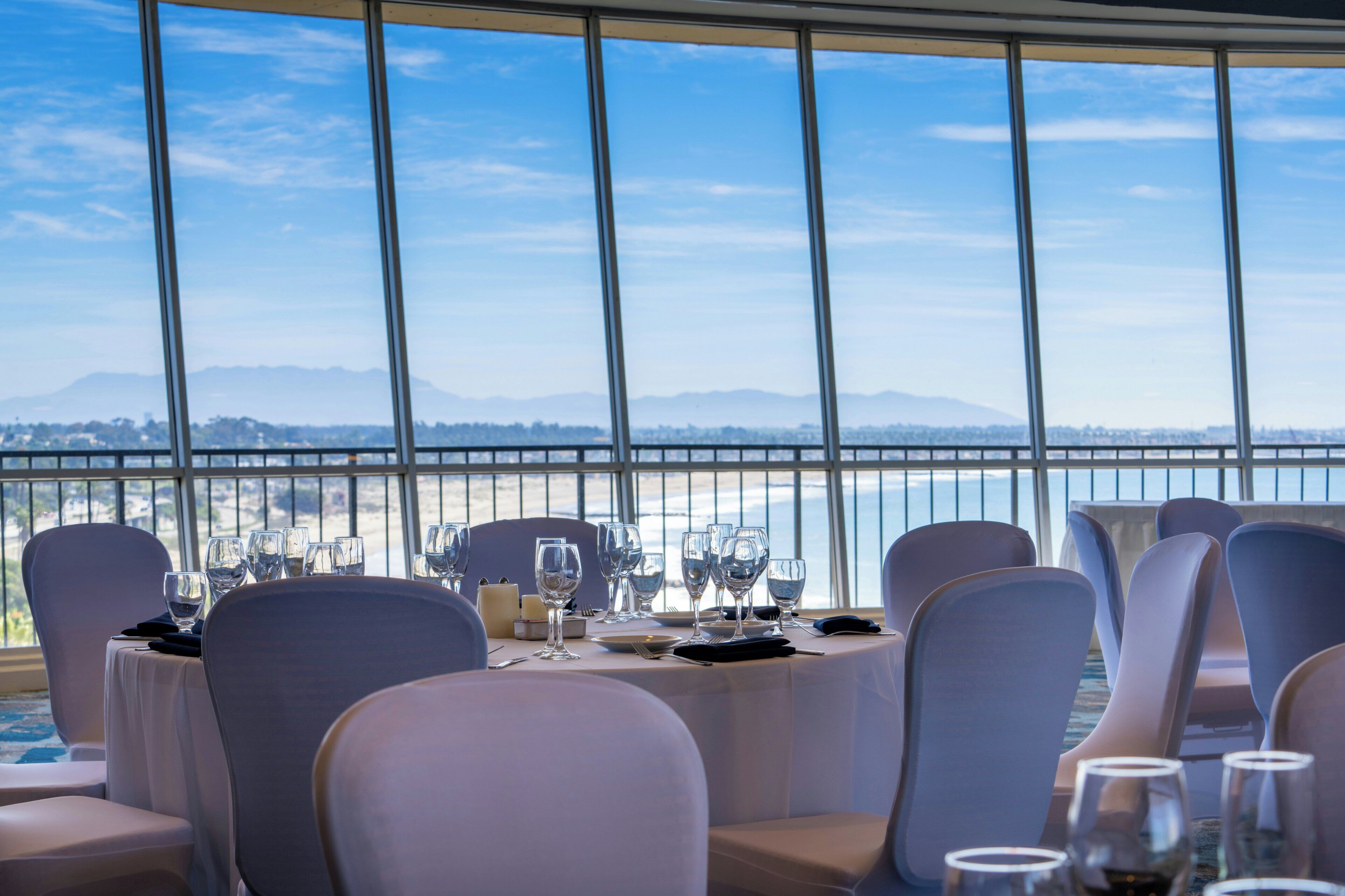 Comedor con mesas redondas, sillas y vista a un cuerpo de agua y montañas.