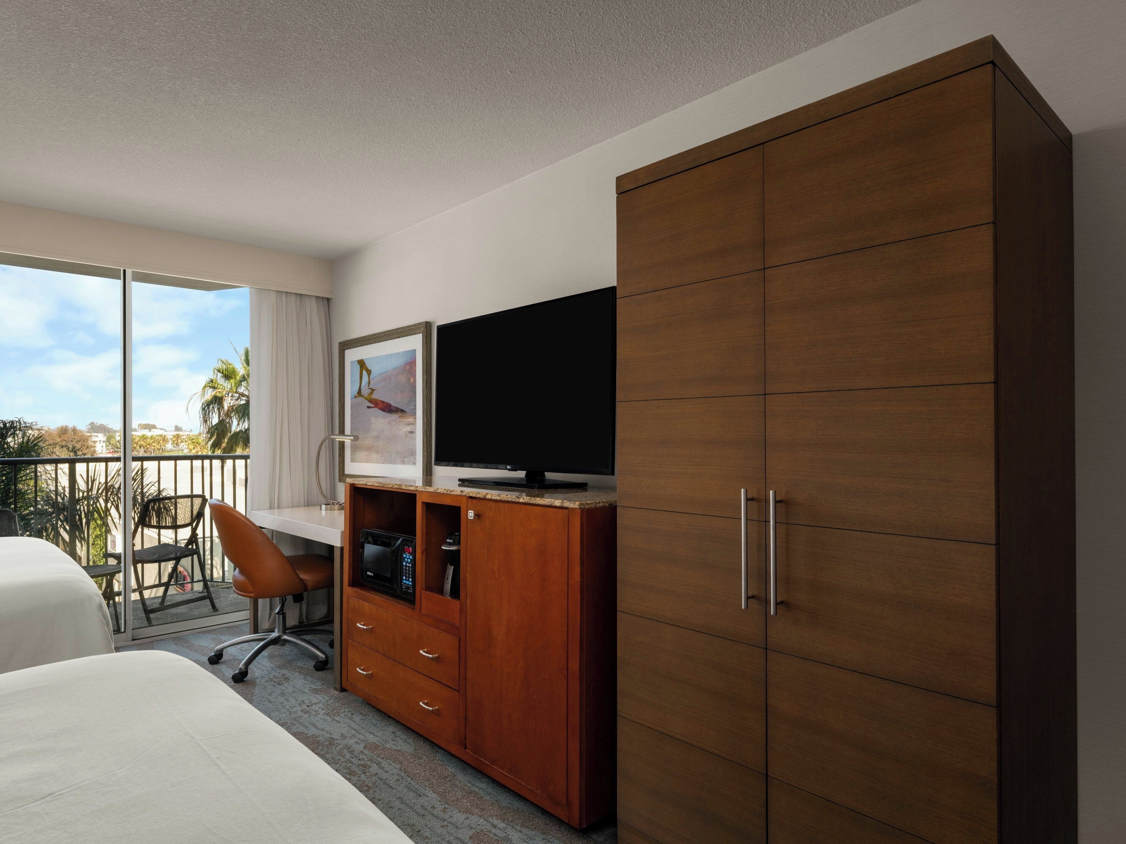 Une chambre d’hôtel comprenant un lit, un bureau avec une chaise, une télévision, une armoire et un balcon avec vue.