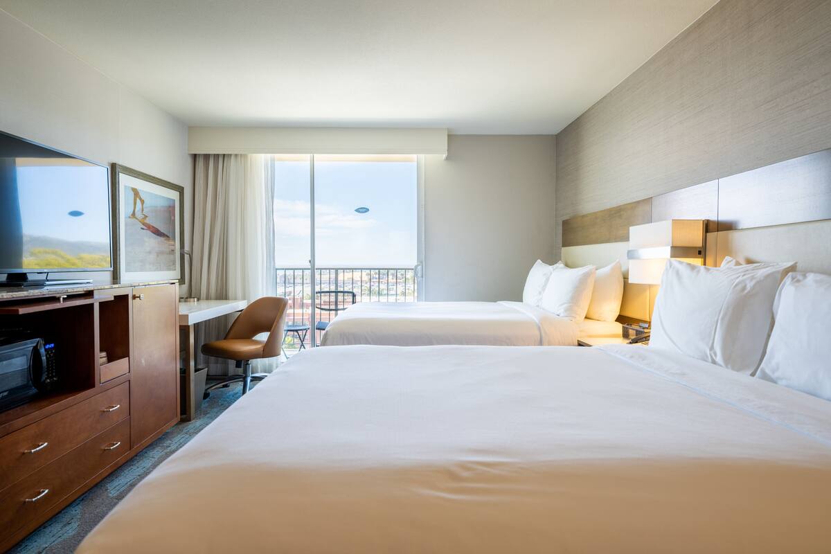A hotel room with two beds, a desk with a computer, a chair, and a TV.