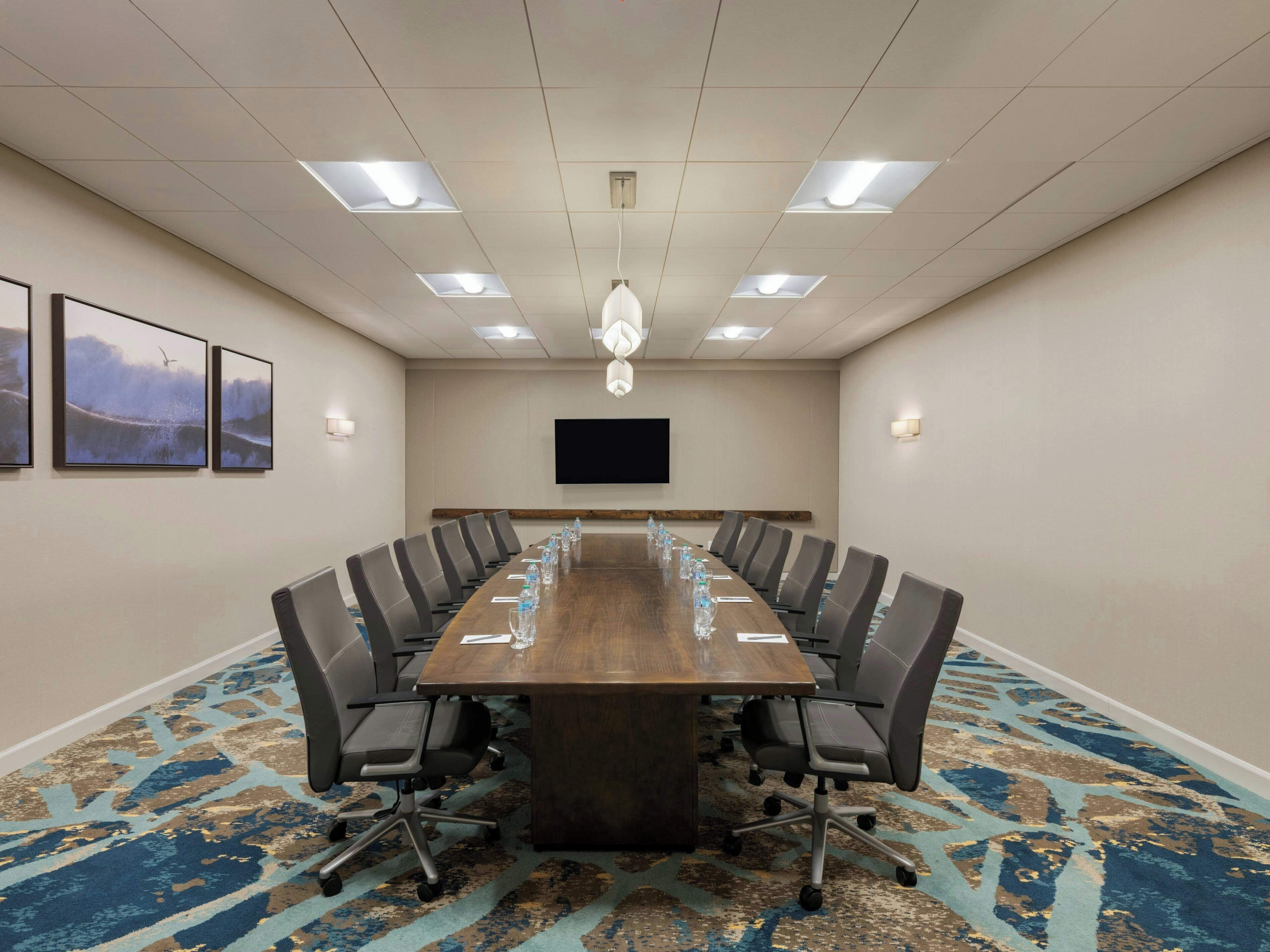 A conference room with a long table, chairs, a flat-screen TV, and a patterned carpet.