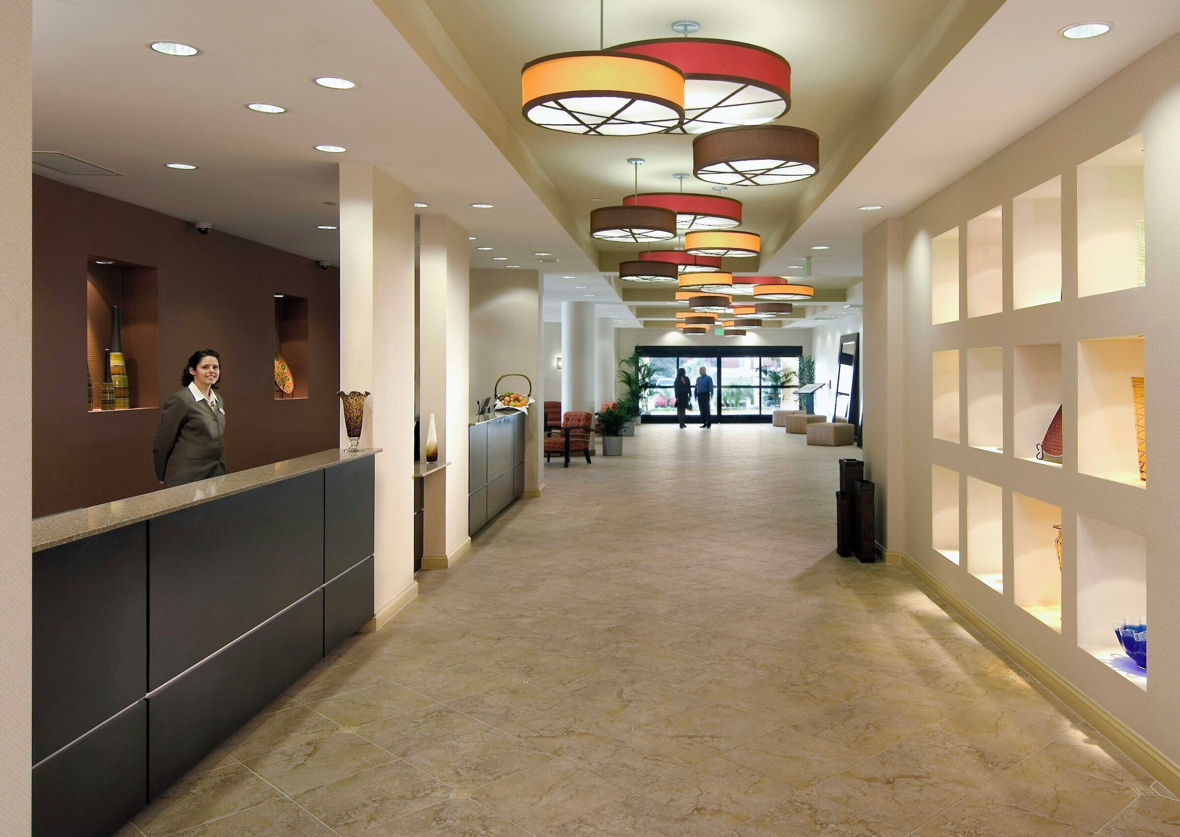 A hotel reception area with a modern design, featuring a reception desk, a seating area, and a corridor leading to the entrance.