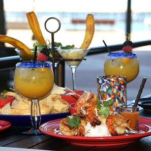 A table with a variety of dishes including shrimp, rice, and chips, along with colorful drinks and a decorative vase. - Crowne Plaza Ventura Beach by IHG (Ventura)