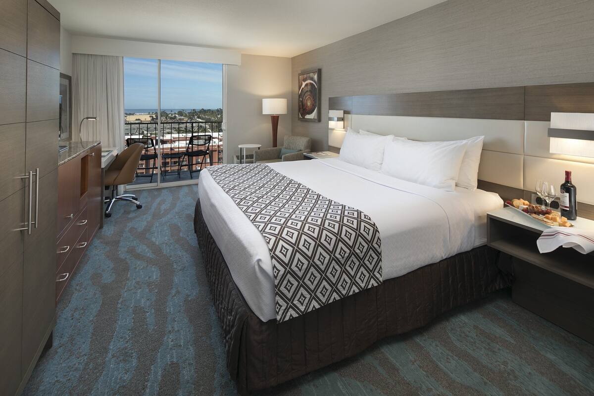 A hotel room with a large bed, a desk, a chair, and a view of the city.