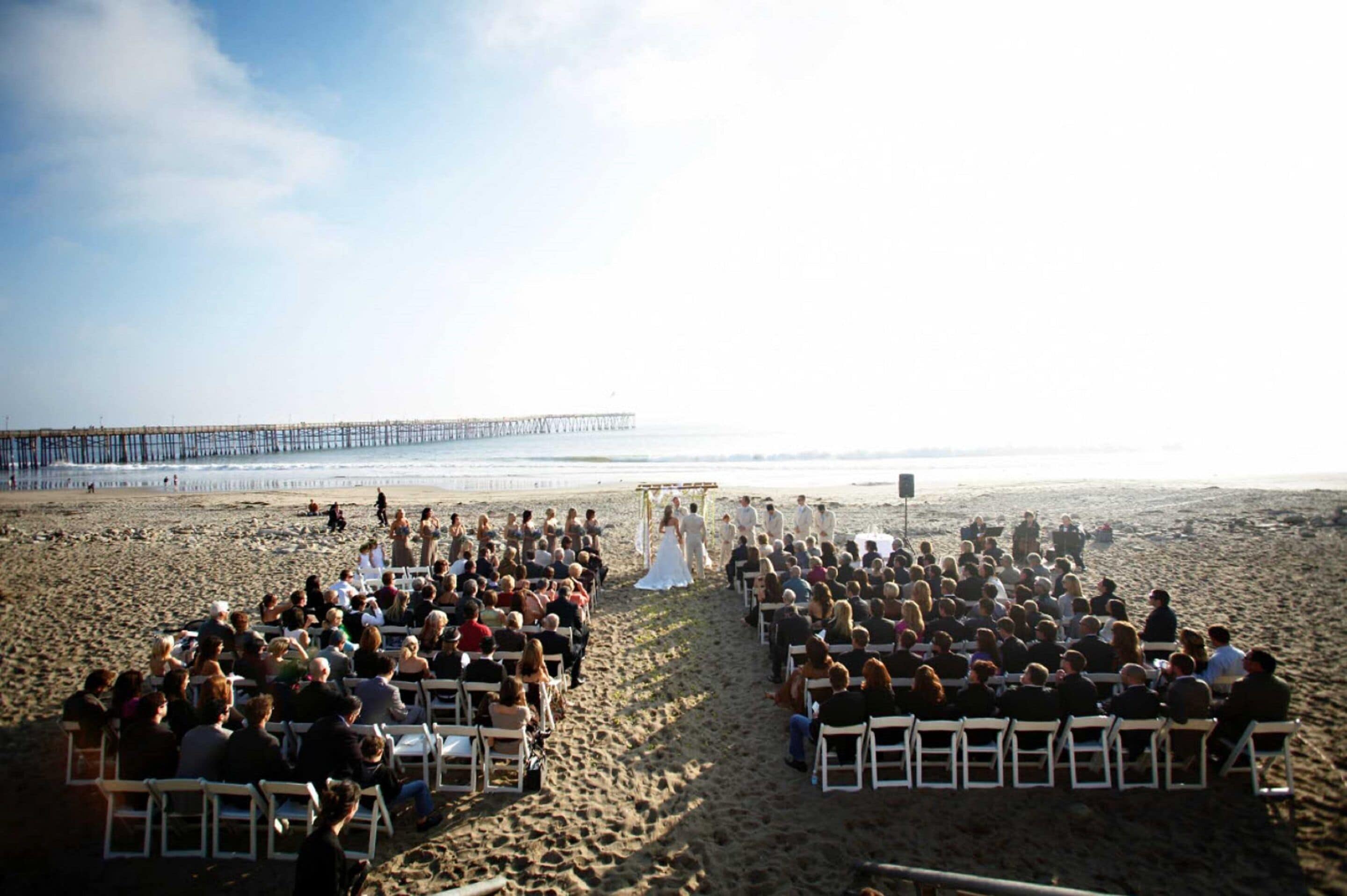 Une cérémonie de mariage sur la plage, les invités étant assis en rangées, face à l’allée.