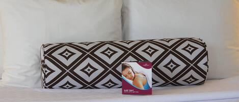A bed with a patterned pillow and a sleep tight package on it.