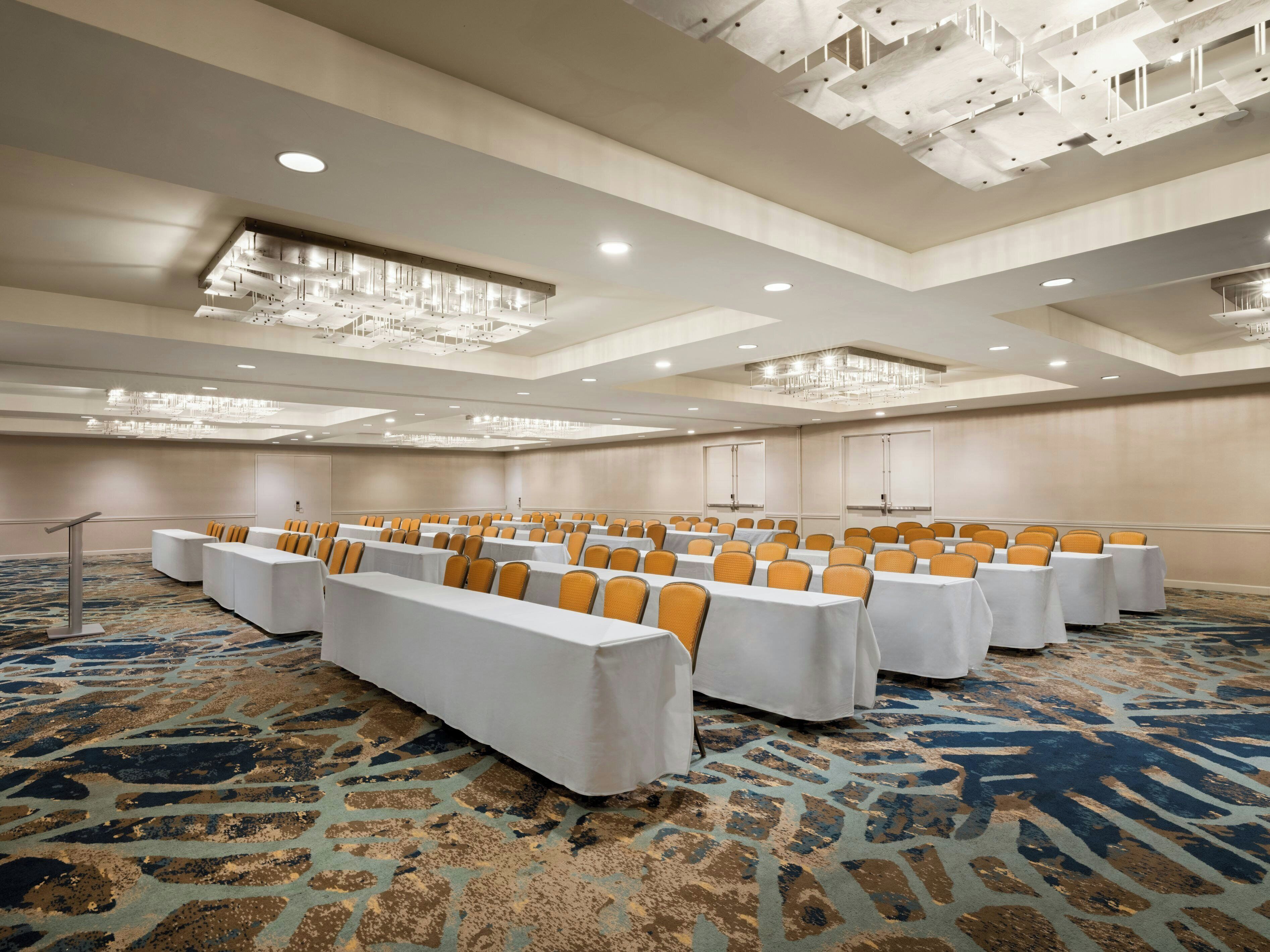 A conference room with rows of tables and chairs, a patterned carpet, and a modern ceiling design.