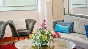 Een moderne woonkamer met een grijze bank, een zwarte fauteuil en een glazen salontafel met een bloemstuk.