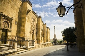 A historic street with stone buildings, a prominent tower, and a street lamp. - NH Córdoba Califa Hotel (Córdoba)