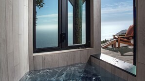 Un moderno espacio de spa con un jacuzzi de paredes de vidrio, terraza de madera y vista al océano.