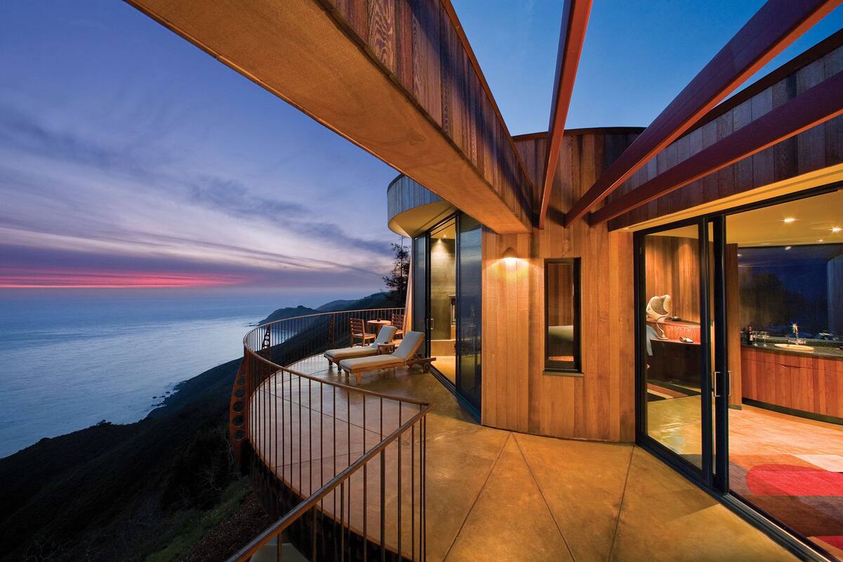 A modern building with a balcony overlooking the ocean at dusk.