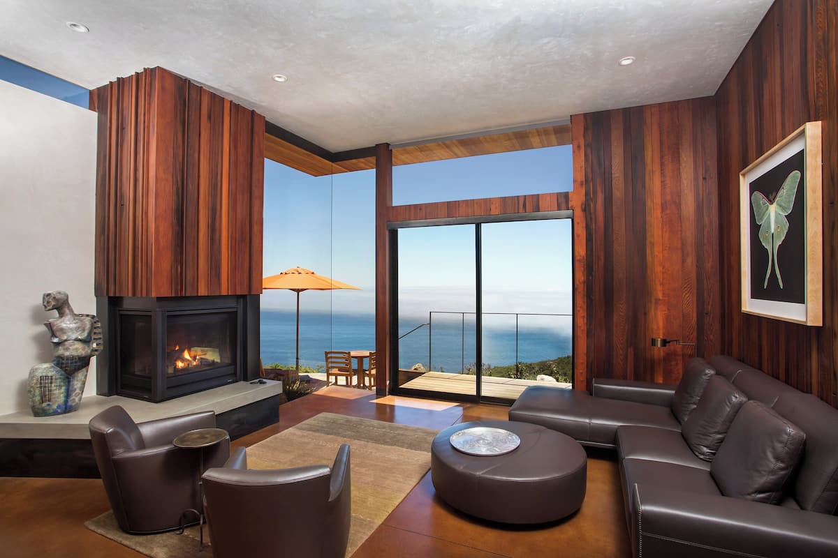 A modern living room with a fireplace, leather furniture, and a view of the ocean.
