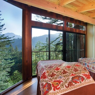 A bedroom with two beds, large windows, a view of mountains, and a stone wall.