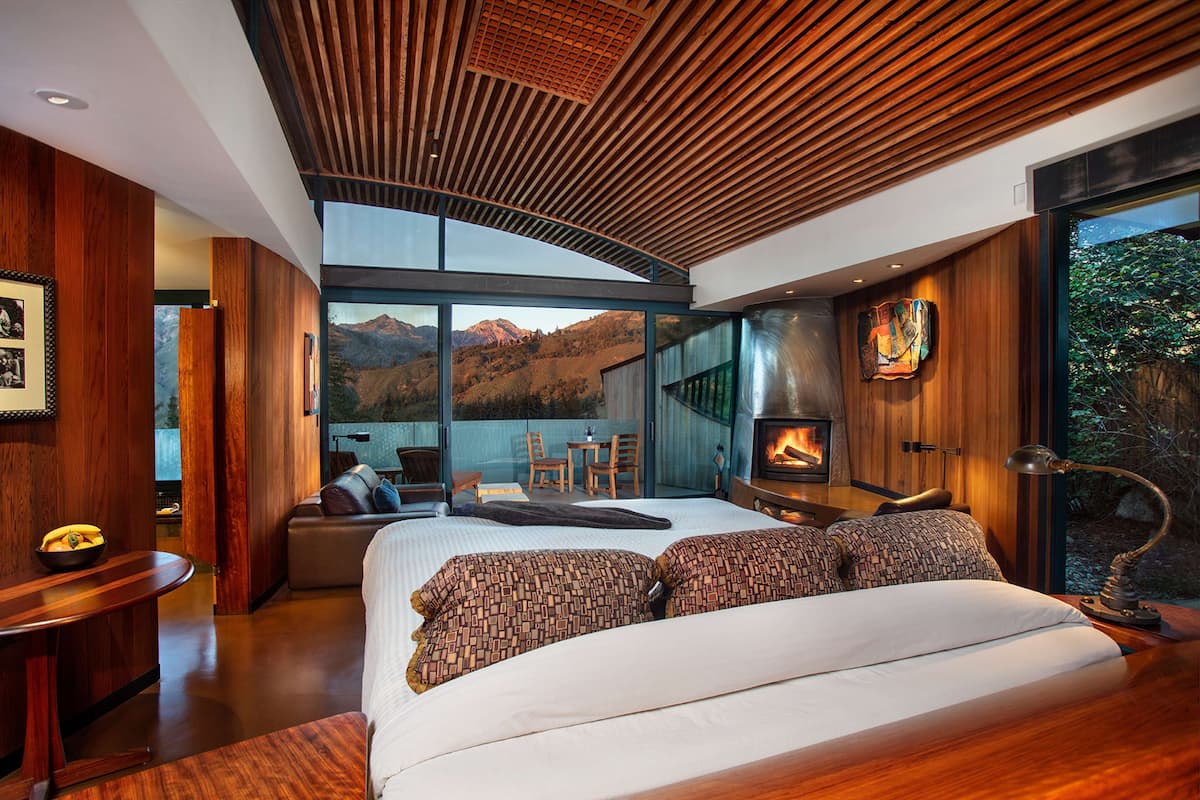 A modern bedroom with a large bed, wooden ceiling, and a view of mountains.