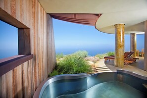 A modern outdoor pool area with a view of the ocean, wooden deck, lounge chairs, and a pergola.