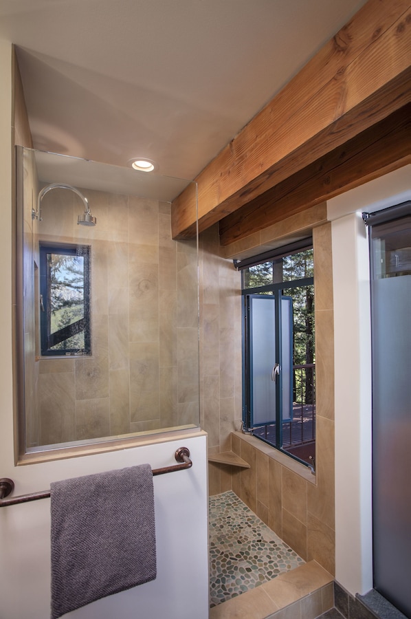 A modern bathroom with a glass shower enclosure, a built-in window, and a wooden ceiling beam. - Post Ranch Inn (Big Sur)