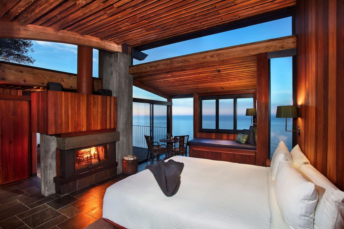 A spacious bedroom with a large bed, a fireplace, and a view of the ocean.