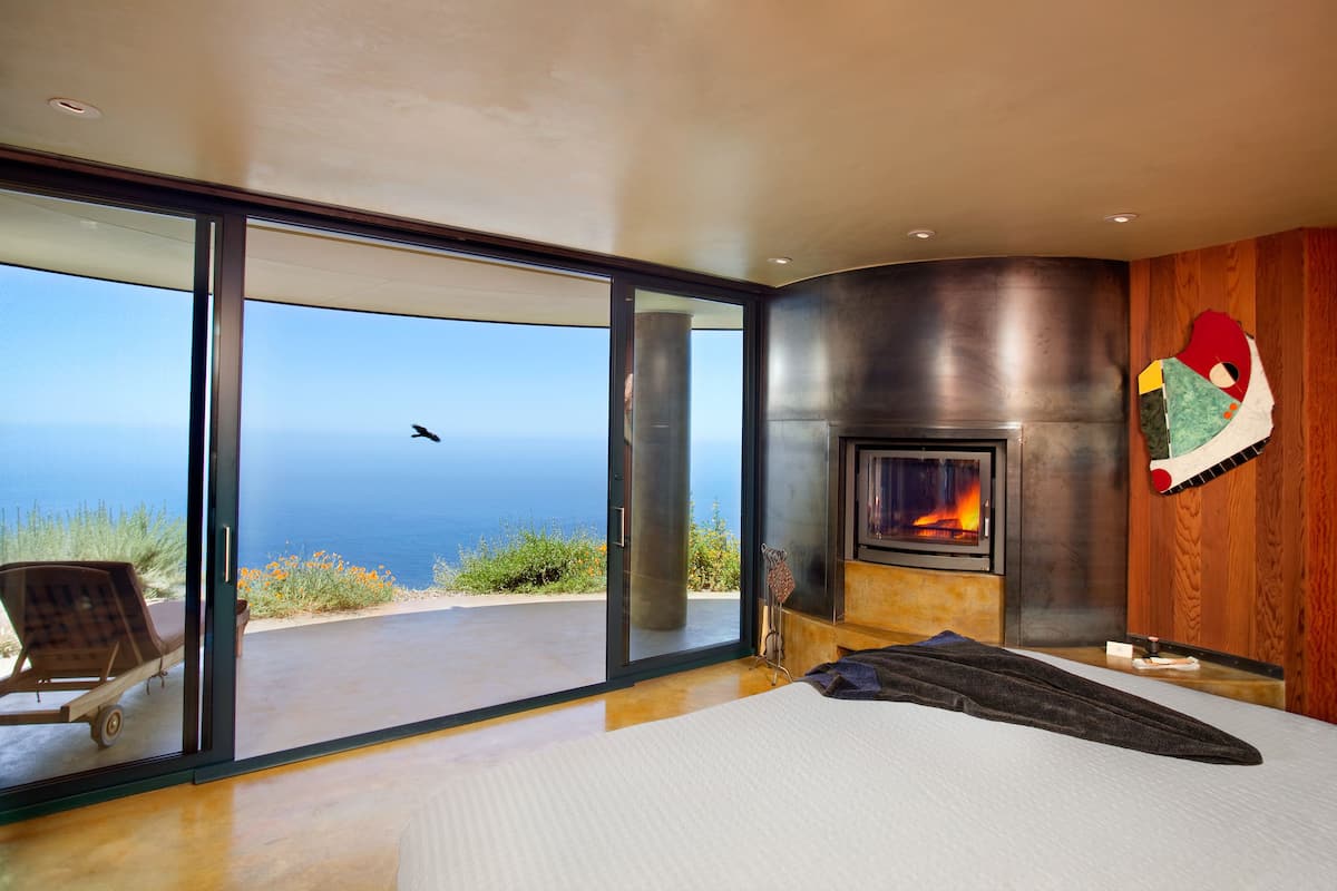 A bedroom with a large sliding glass door leading to a balcony with a view of the ocean.