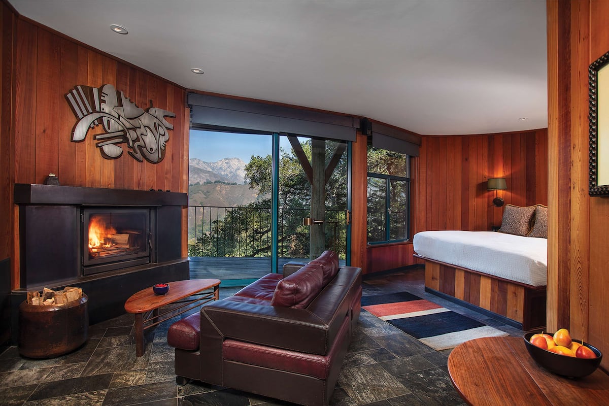 A cozy living room with a fireplace, leather sofa, and a large window offering a mountain view.