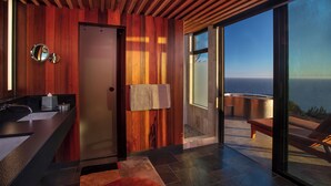 A modern bathroom with a wooden panel wall, a glass shower enclosure, and a view of the ocean.