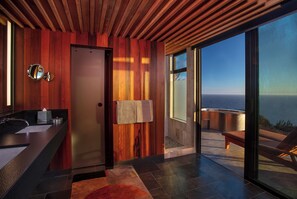 A modern bathroom with a wooden panel wall, a glass shower enclosure, and a view of the ocean.