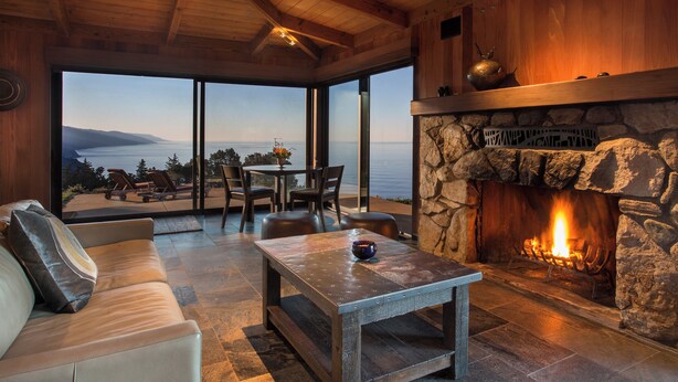 Una sala de estar acogedora con chimenea de piedra, un ventanal con vistas panorámicas y asientos cómodos.