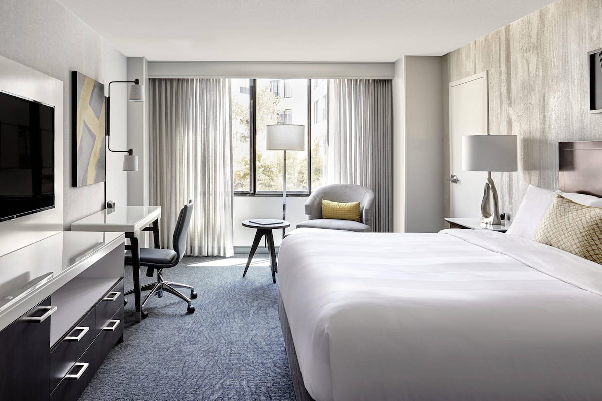 A hotel room with a bed, a desk, a chair, a TV, and a window with curtains.