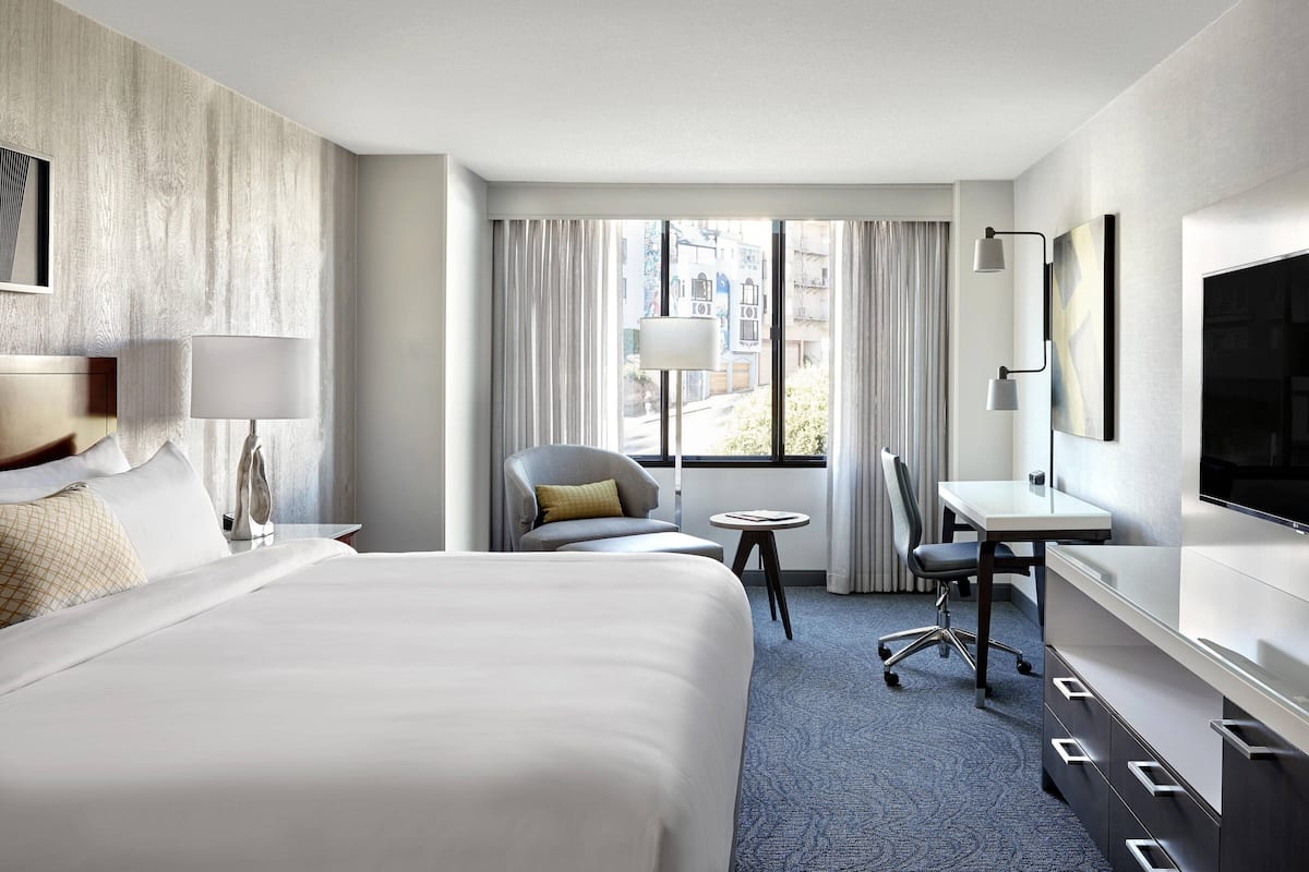 A hotel room with a large bed, a desk, a chair, a TV, and a window with curtains.