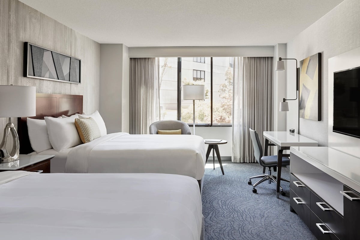 A hotel room with two beds, a desk, a chair, a TV, and a window with curtains.