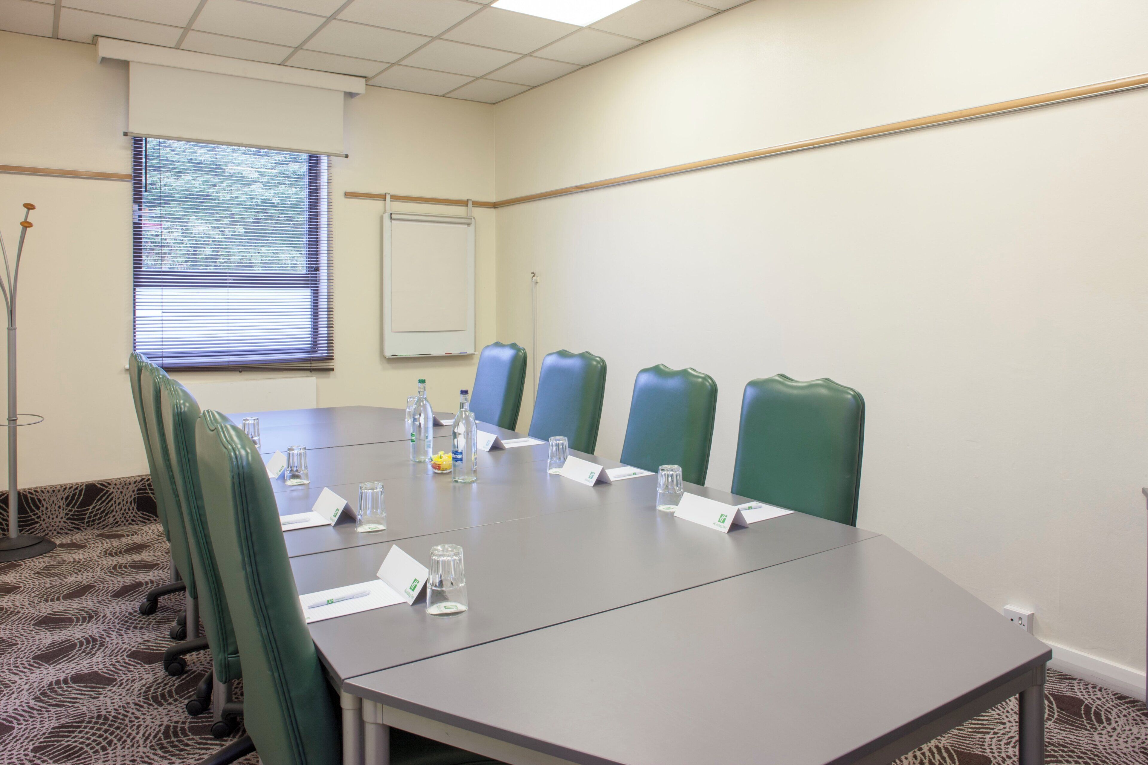 Un salón de conferencias con una larga mesa, sillas verdes y una pizarra.