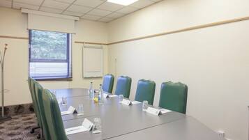 Un salón de conferencias con una larga mesa, sillas verdes y una pizarra.