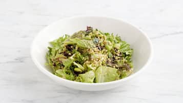 A white bowl containing a salad with various greens and grains on a marble surface.