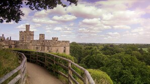 A historic castle with a paved pathway leading to it, surrounded by lush greenery and a cloudy sky. - Holiday Inn Leamington Spa - Warwick by IHG (Warwick)