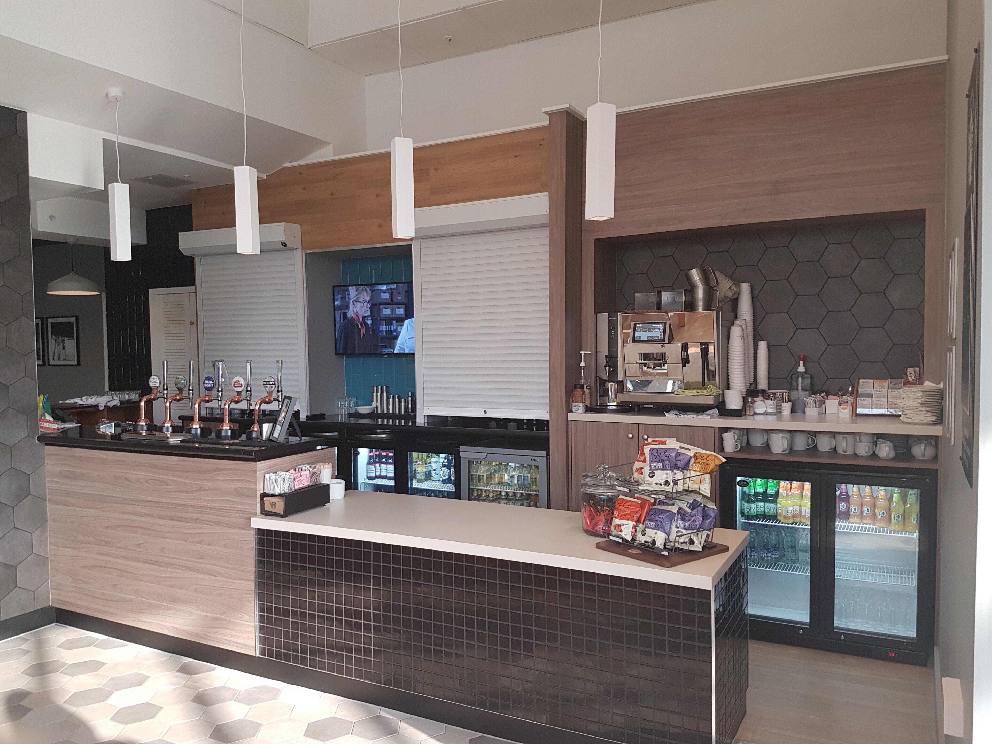 Zona de bar moderna con una máquina de café, dispensadores de bebidas y una vitrina refrigerada.