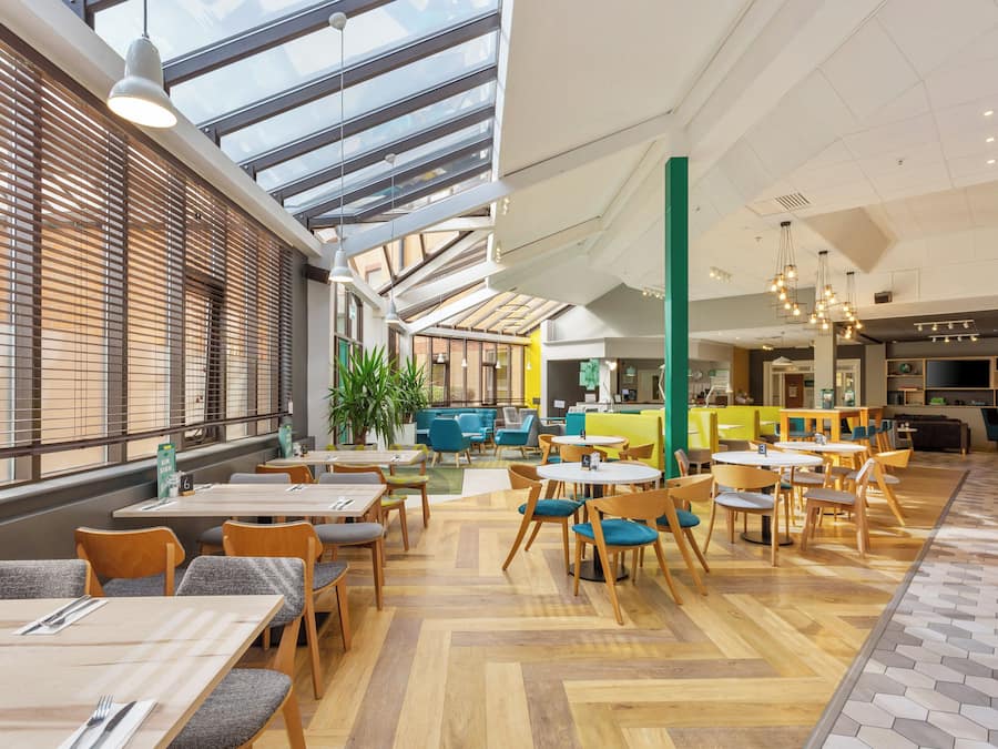 A spacious indoor area with multiple seating arrangements, including tables and chairs, and a high ceiling with skylights.