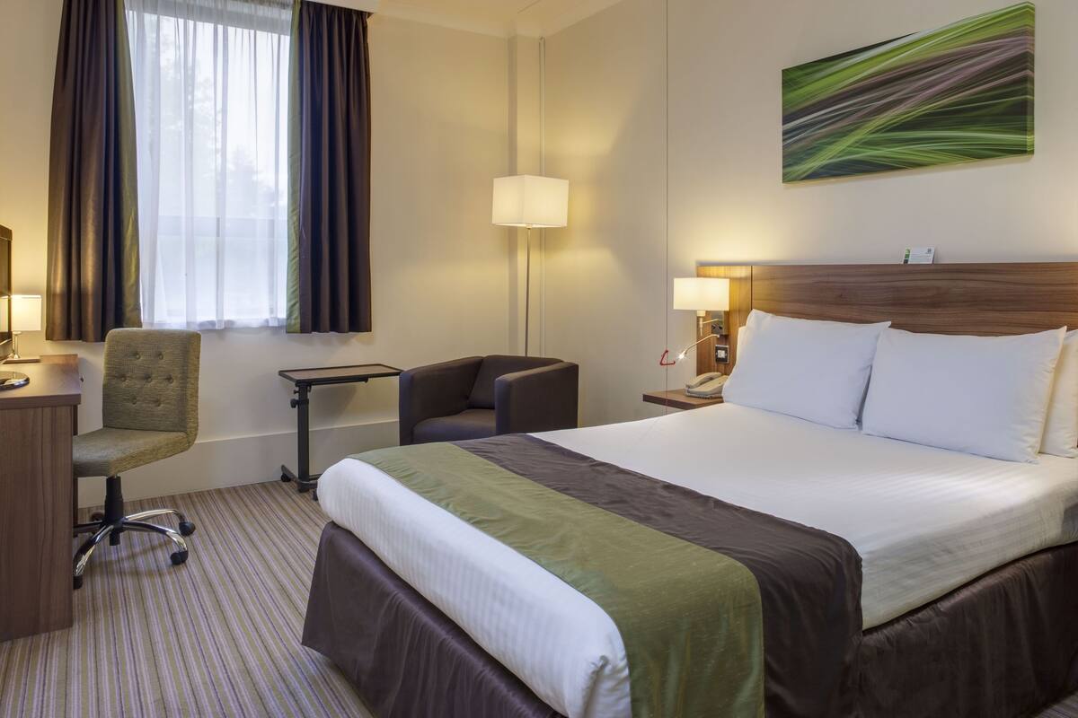 Une chambre d’hôtel avec un grand lit, un bureau, une chaise, une lampe et un tableau au mur.
