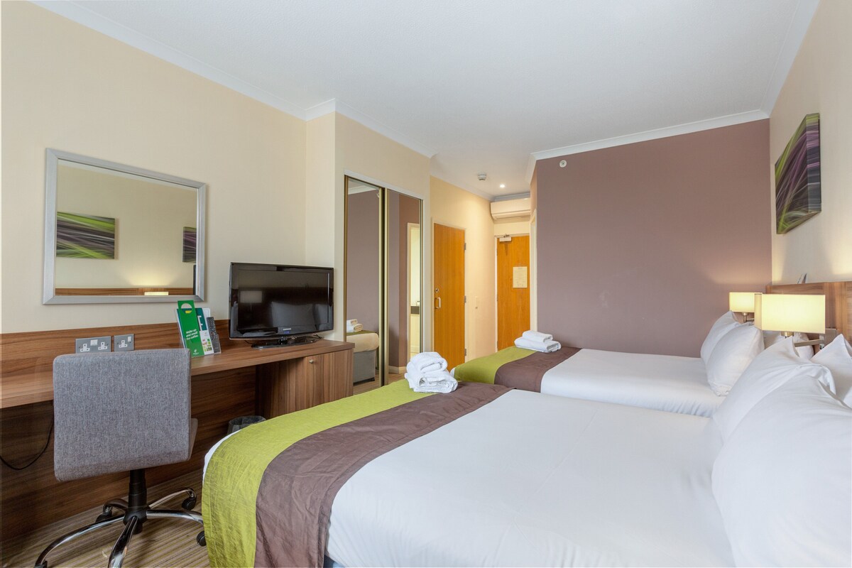 A hotel room with two beds, a desk with a television, a chair, and a mirror.