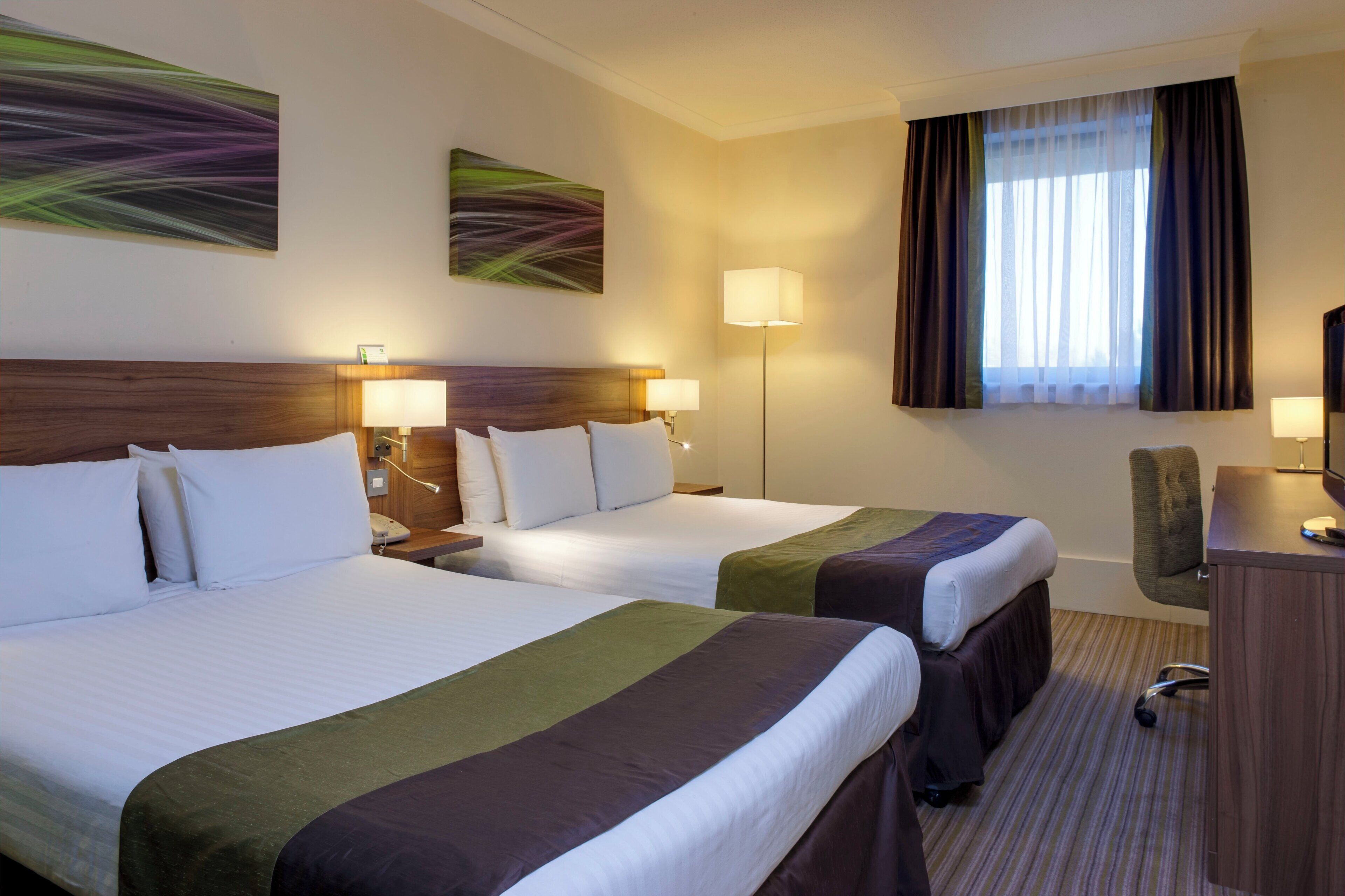 A hotel room with two beds, a desk, a chair, and a window with curtains.