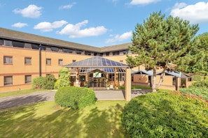 A Holiday Inn hotel with a central courtyard, a large tree, and a well-maintained lawn.