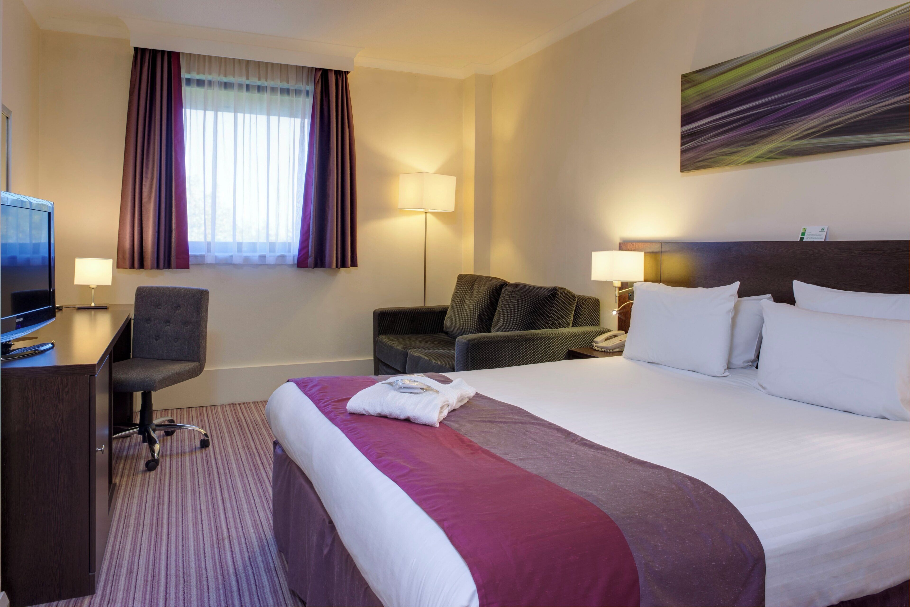 A hotel room with a bed, a desk, a chair, a television, and a window with curtains.