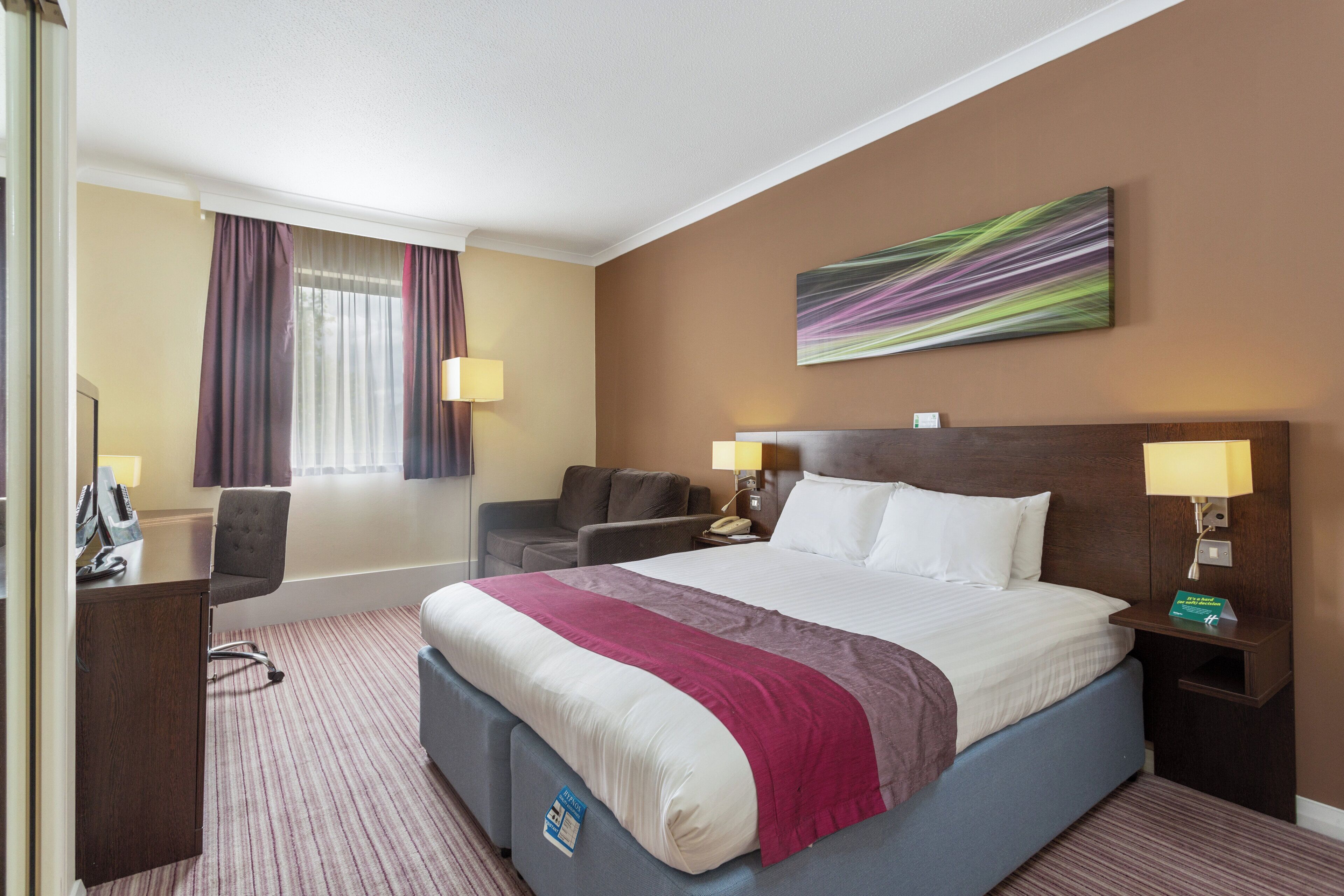 A hotel room with a large bed, a desk, a chair, a sofa, and a painting on the wall.