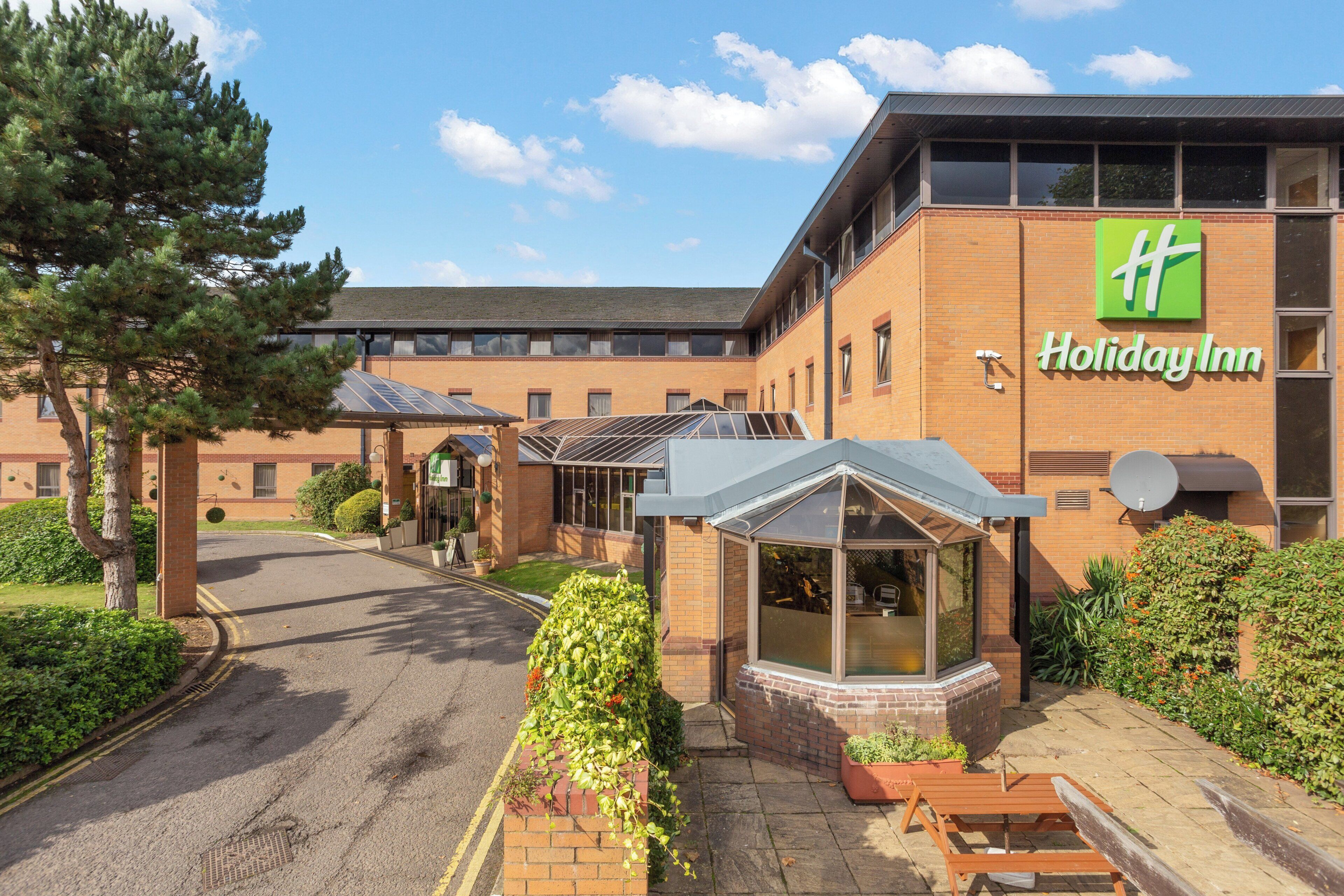 A Holiday Inn hotel with a brick facade, a covered outdoor seating area, and a clear sky.