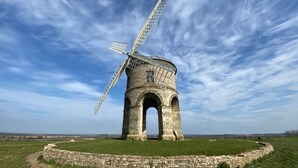A historic windmill with a large sail, standing on a grassy mound with a stone base, surrounded by open fields. - Holiday Inn Leamington Spa - Warwick by IHG (Warwick)