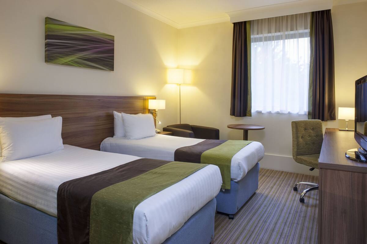 Une chambre d’hôtel avec deux lits, un bureau, une chaise, une lampe et un téléviseur.