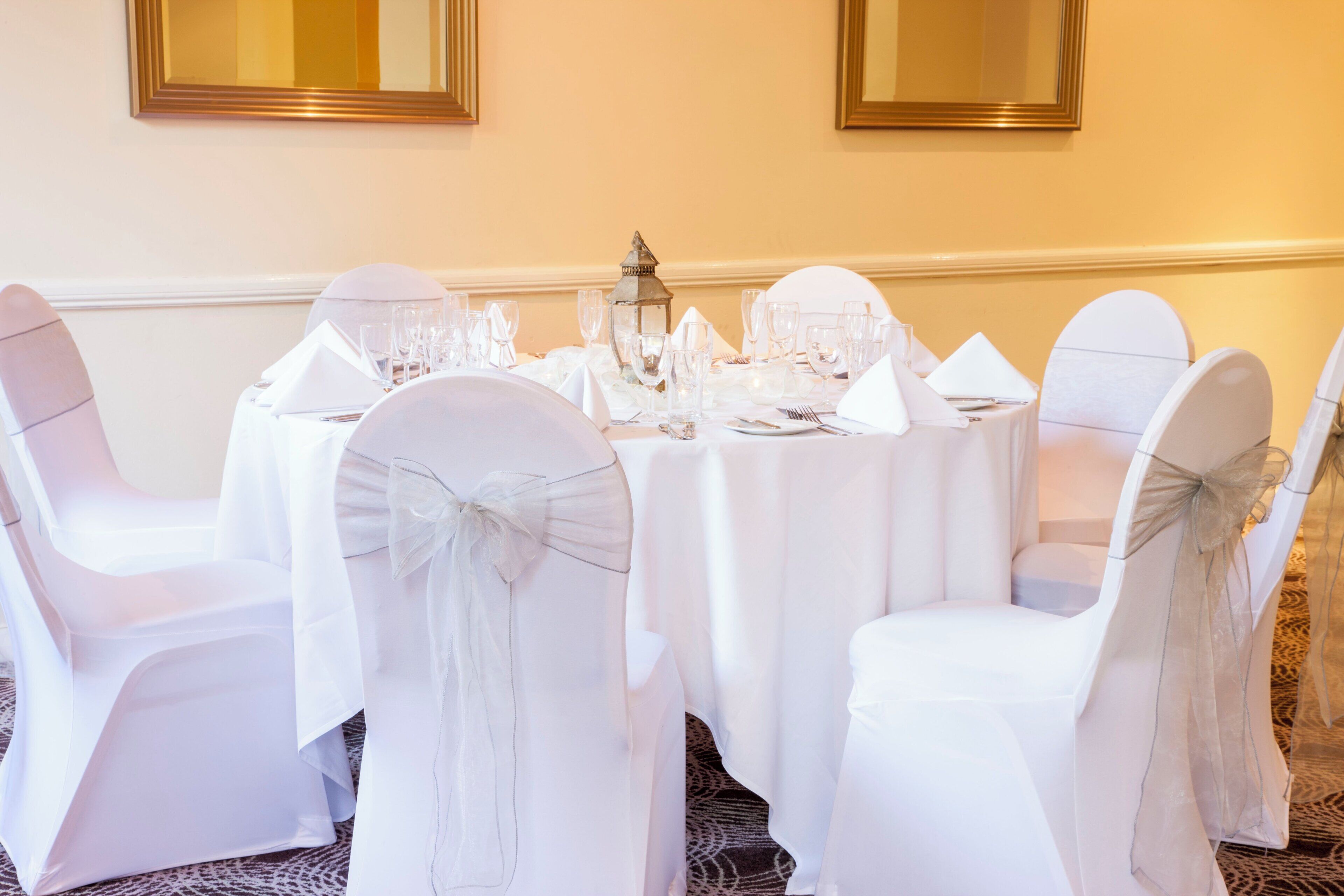 A round table set for a formal event with white chairs and a white tablecloth.