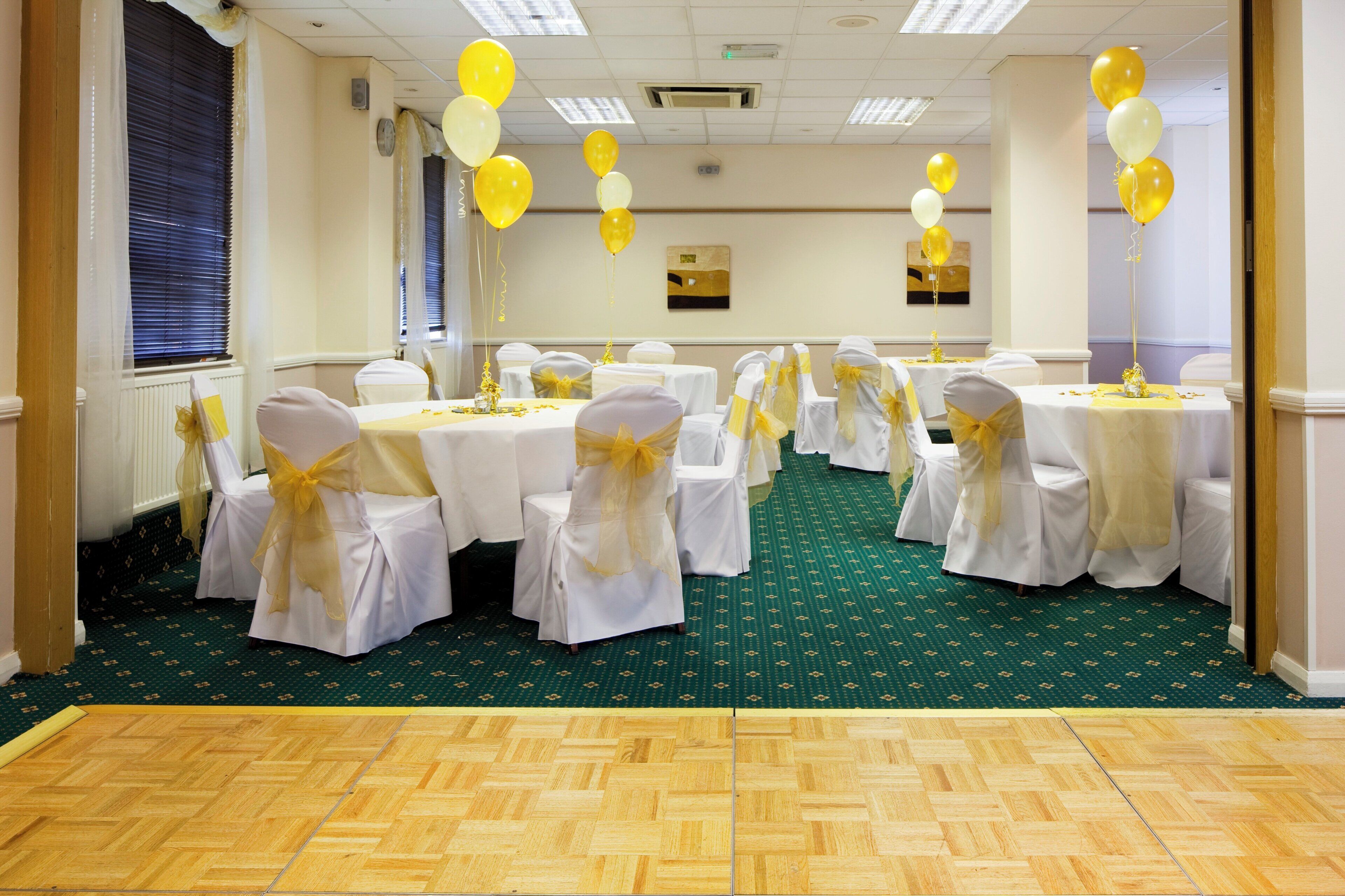A conference room with round tables, white chairs, and yellow sashes.
