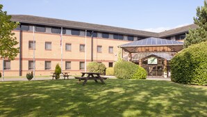A building with a brick facade, a covered outdoor seating area, and a sign for a hotel. - Holiday Inn Leamington Spa - Warwick by IHG (Warwick)