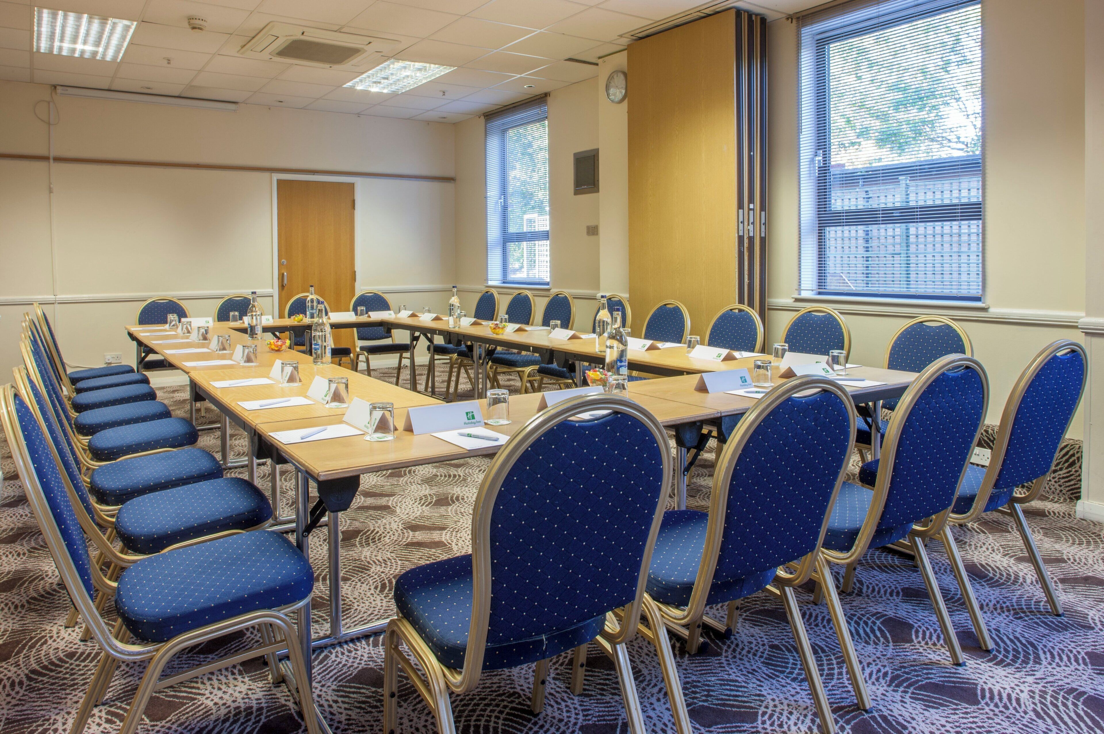 A conference room with a long table, blue chairs, name cards, and a clock on the wall.