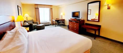 A hotel room with a large bed, a desk, a chair, a television, and a dresser.